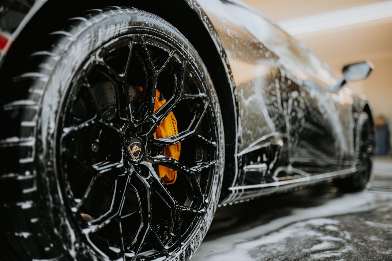 hero-img-01 Detailed close-up of a luxury car wheel covered in soap suds during a professional car wash.