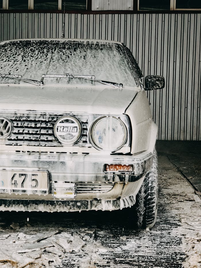 gallery-4 Close-up of a classic Volks-wagen covered in soap foam during a car wash in a garage.