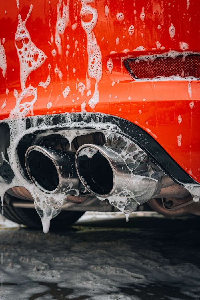 gallery-1 Detailed view of a red sports car exhaust pipe covered in foam at a car wash.