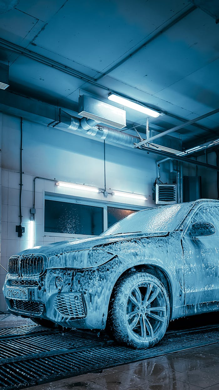 gallery-3 Luxury SUV covered in foam inside a modern car wash station enhanced by blue lighting.