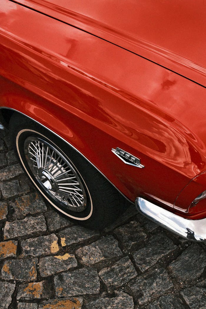 gallery-5 Close-up of a classic red car's wheel on cobblestone, showcasing vintage style.