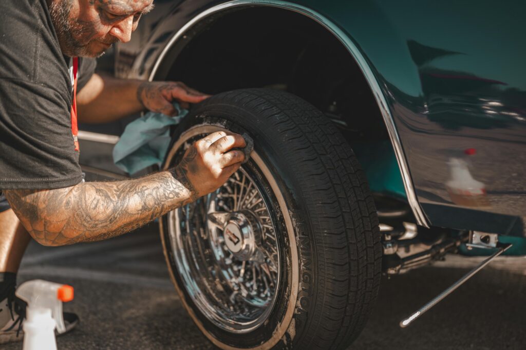 pexels-photo-35244783-35244783 A man with tattoos polishes a classic car wheel, focusing on tire cleaning.