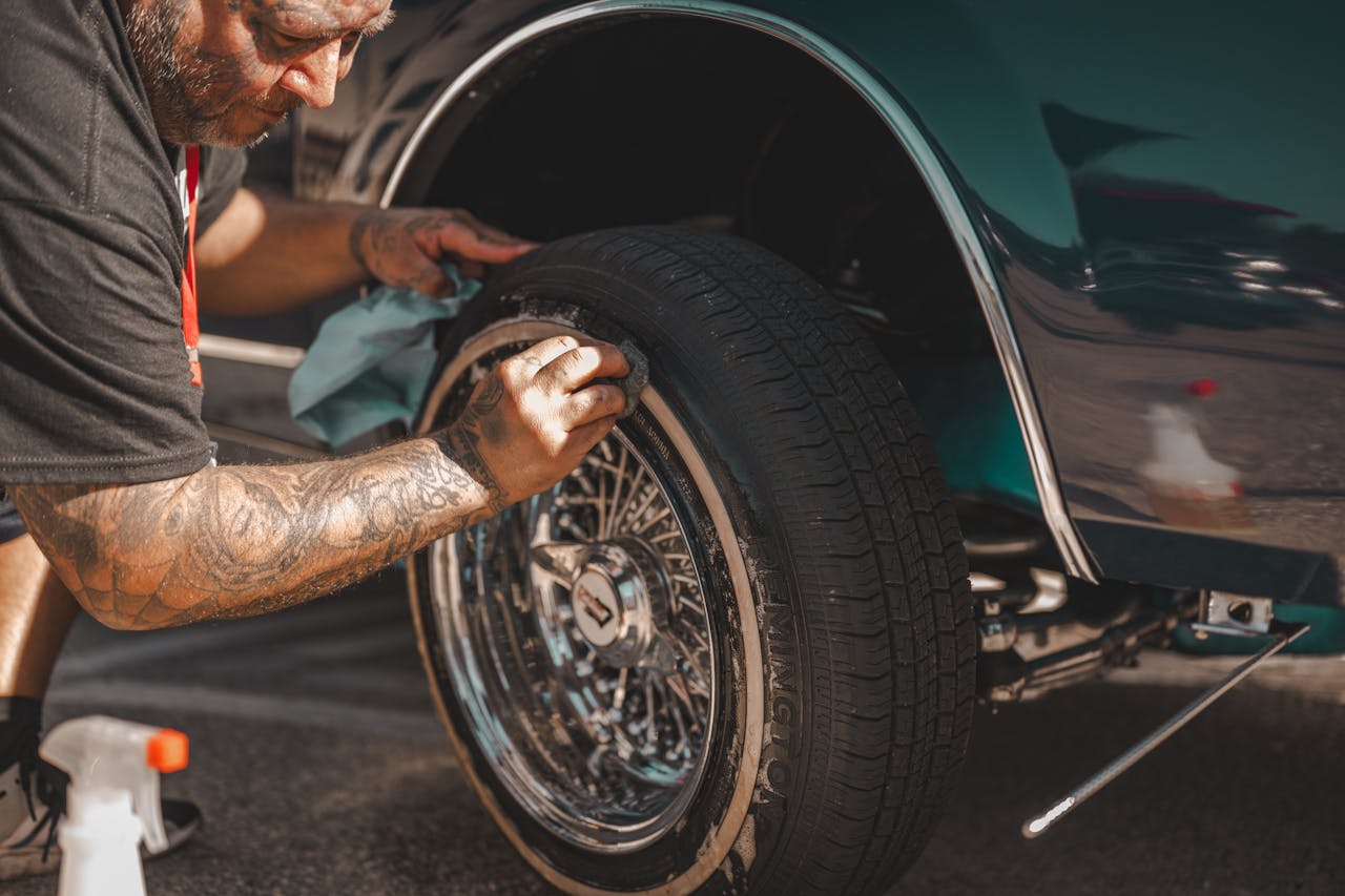 gallery-2 A man with tattoos polishes a classic car wheel, focusing on tire cleaning.