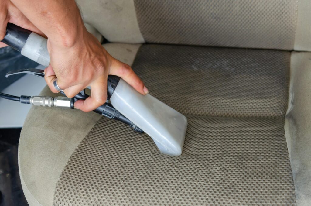 pexels-photo-5233285-5233285 Hands using a vacuum nozzle to deeply clean a fabric car seat, removing dirt and stains.