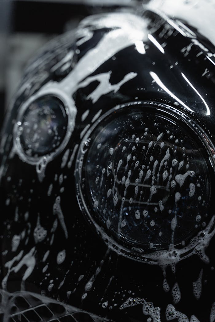 services-02 A detailed close-up of a car headlight covered with soap suds during a wash.